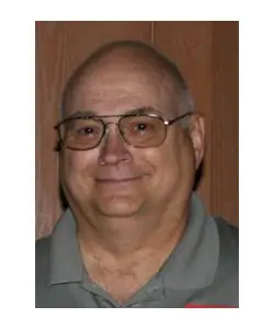 A man with glasses and a beard wearing a gray shirt.