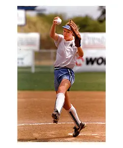 A woman in white shirt and blue shorts playing baseball.