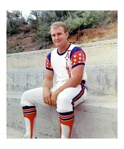 A man sitting on the side of a wall wearing white and orange.