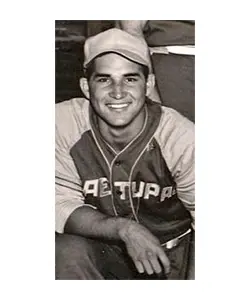 A man in a baseball uniform sitting on the ground.