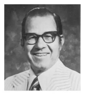 A man in glasses and a tie is smiling.